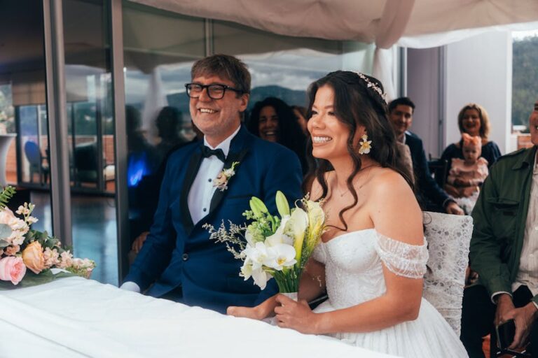 Smiling bride and groom sitting at a wedding ceremony with guests around.