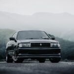 A black sports car parked on a scenic mountain road enveloped in mist, creating a dramatic and moody atmosphere.