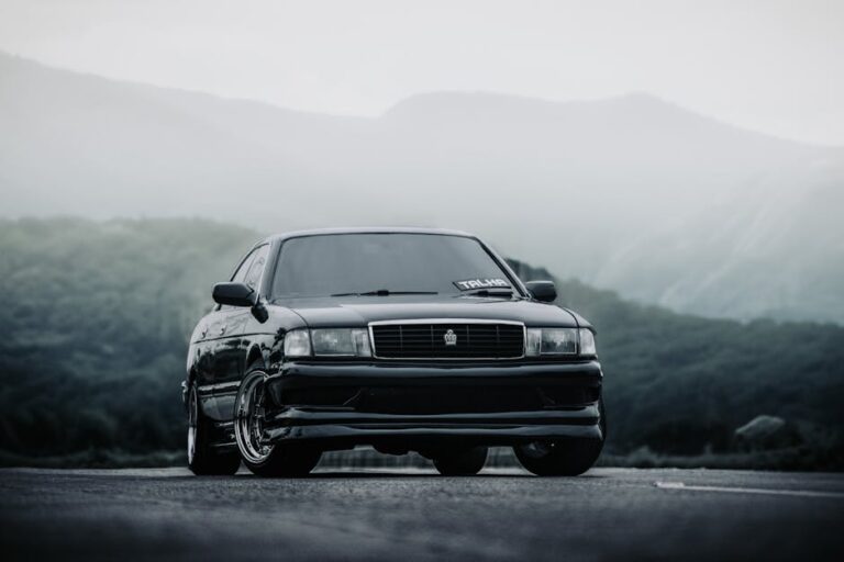 A black sports car parked on a scenic mountain road enveloped in mist, creating a dramatic and moody atmosphere.