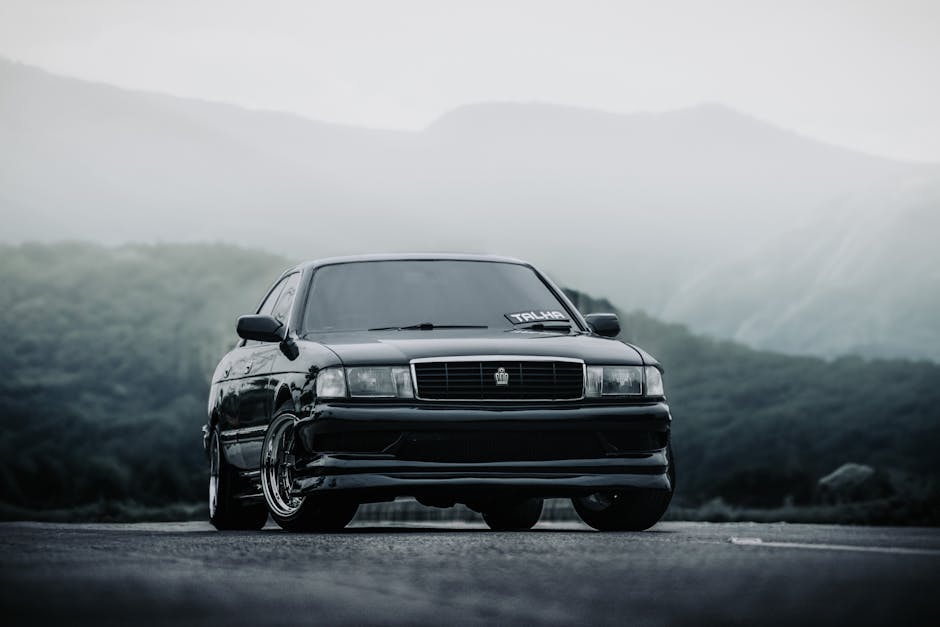 A black sports car parked on a scenic mountain road enveloped in mist, creating a dramatic and moody atmosphere.