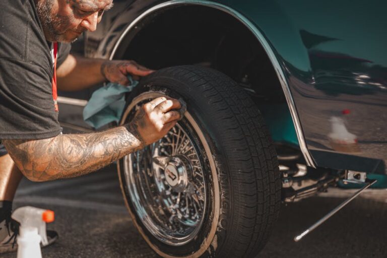 A man with tattoos polishes a classic car wheel, focusing on tire cleaning.