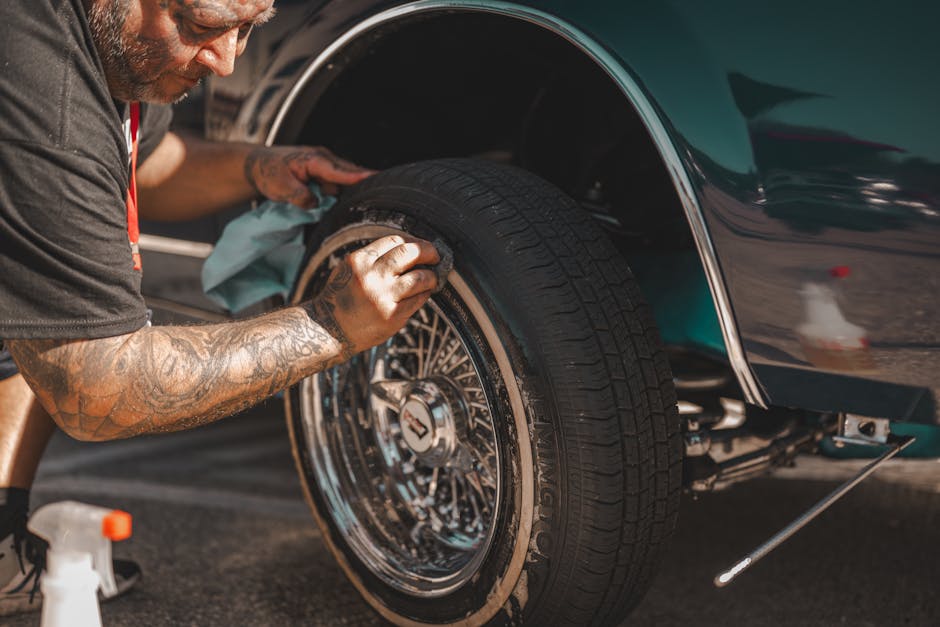 A man with tattoos polishes a classic car wheel, focusing on tire cleaning.