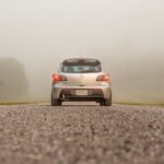 Silver car on a fog-covered gravel road, showcasing transportation in serene mist.