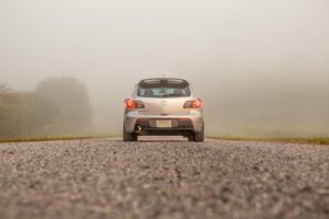 Silver car on a fog-covered gravel road, showcasing transportation in serene mist.