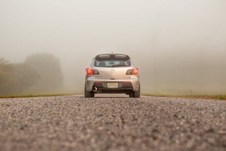 Silver car on a fog-covered gravel road, showcasing transportation in serene mist.
