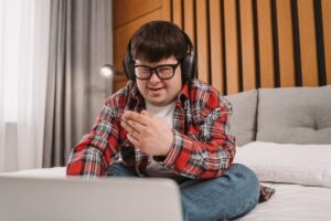 Smiling young man with Down syndrome using laptop and headphones indoors.