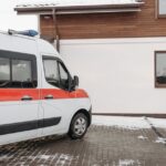 Ambulance vehicle parked outside a house in a snowy winter setting.
