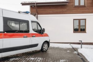 Ambulance vehicle parked outside a house in a snowy winter setting.