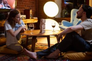 Couple enjoying a relaxed evening playing a board game with wine in a cozy home setting.
