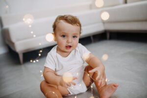 Cute baby sitting on the floor with string lights, in a cozy indoor setting.