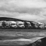 Row of parked semi trucks in a rainy lot, captured in a dramatic black and white setting.
